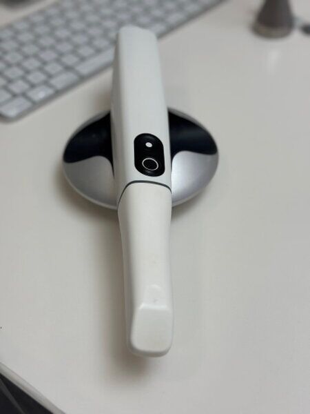 Ein Intraoralscanner in seiner Ladestation auf einem weißen Tisch liegend neber der Tastatur.